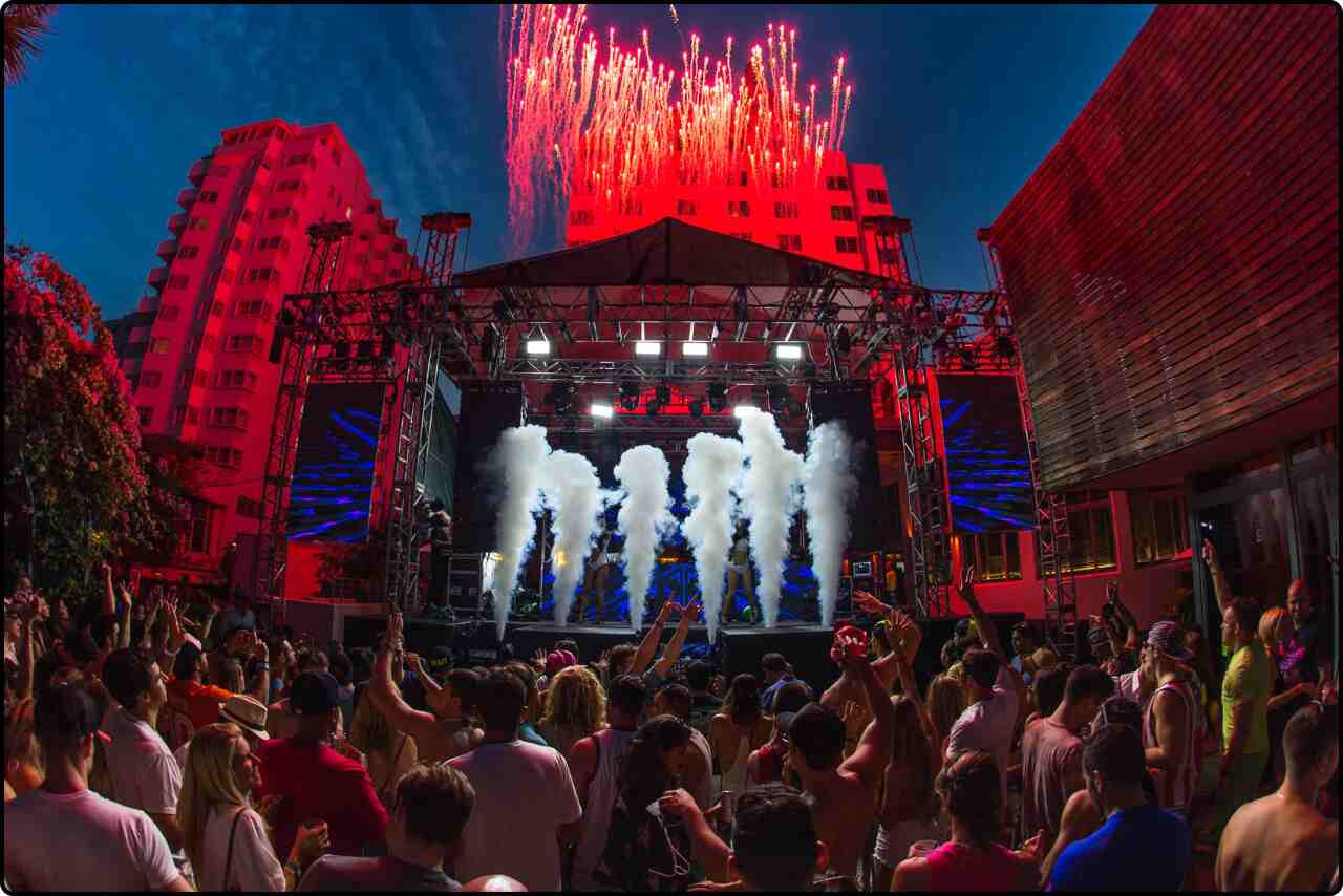 Festival-goers dancing joyfully near a stage illuminated by vibrant nighttime lights